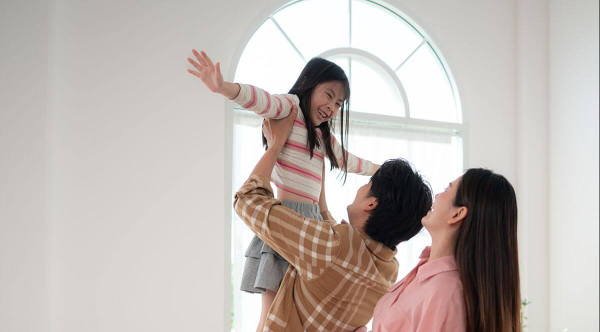 Parents lifting their young daughter in a bright condominium interior, representing a safe and nurturing family home.