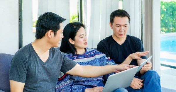 Three adults discussing information on a laptop and tablet in a bright residential lounge, representing personalized lifestyle support and convenience
