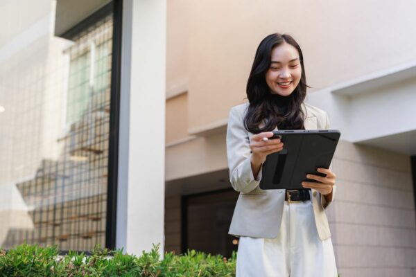 Woman using a tablet outside a modern building, representing property research and the market appeal of residences with city view